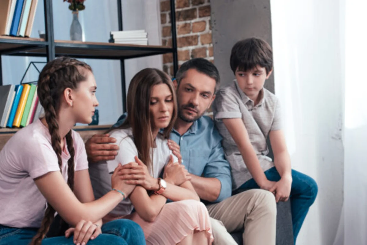 family embracing and cheering up frustrated woman on sofa in counselor office
